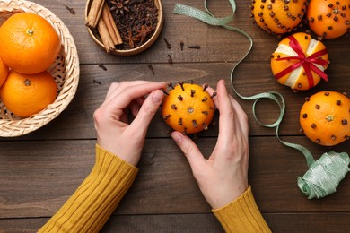 Woman decorating fresh tangerine with cloves at wooden table, top view