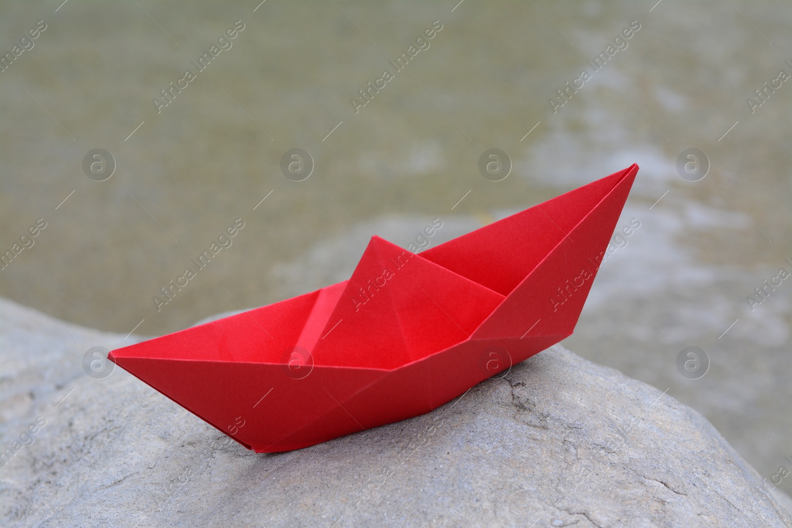 Photo of Beautiful red paper boat on stone outdoors, closeup