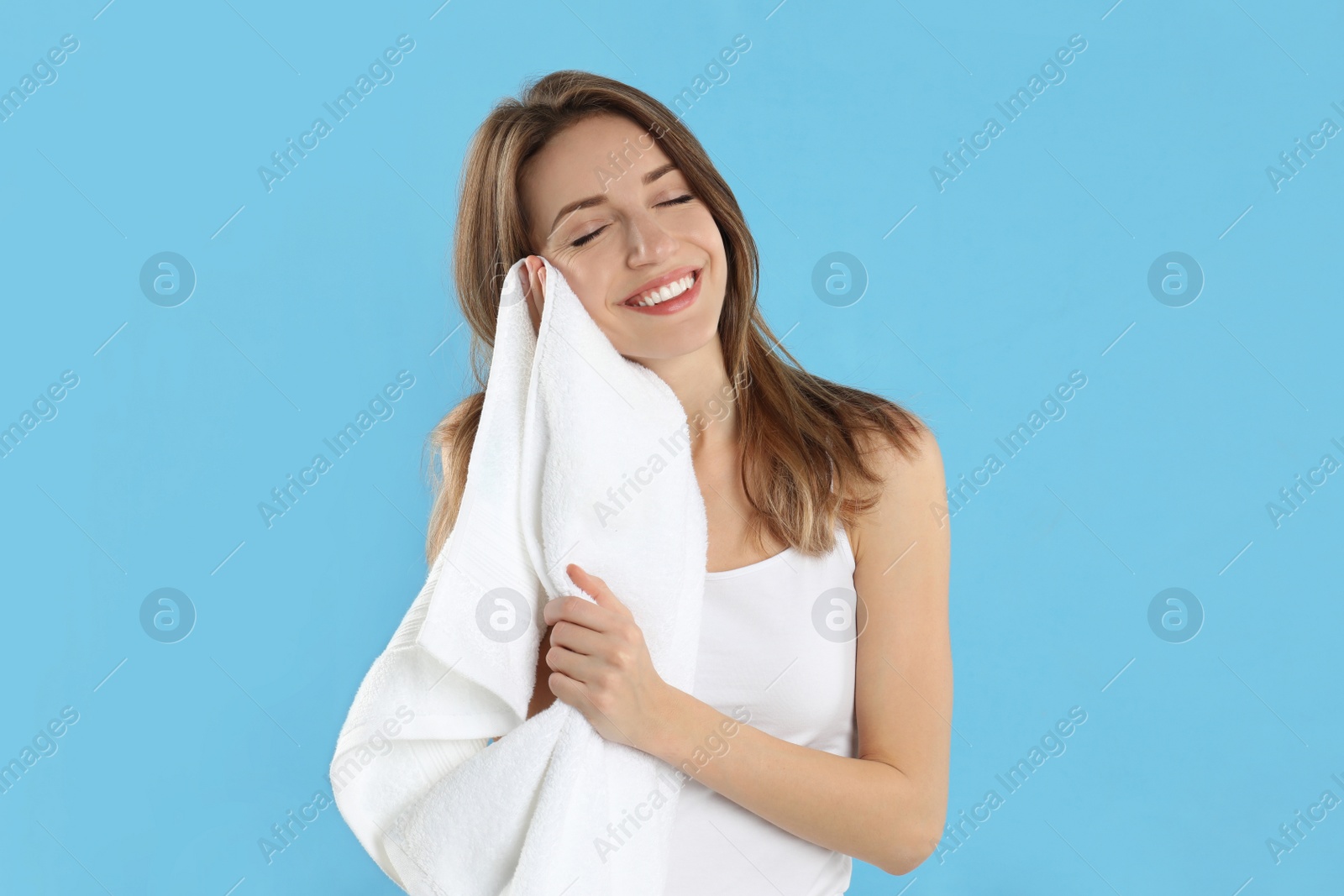 Photo of Young woman wiping face with towel on light blue background