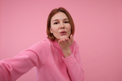 Beautiful woman taking selfie on pink background