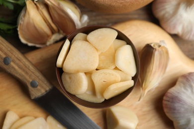 Photo of Fresh sliced garlic cloves in bowl on wooden table, flat lay. Organic product