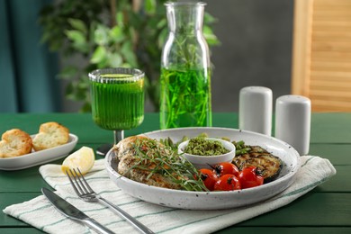 Photo of Tasty chicken, vegetables with tarragon and pesto sauce served on green wooden table