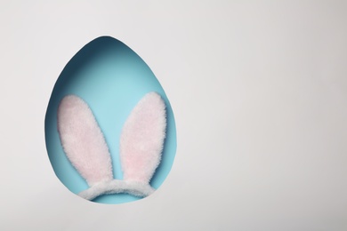 Photo of Top view of Easter bunny ears headband on color background through egg shaped hole, space for text