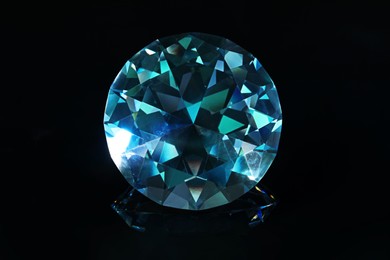 Photo of Beautiful dazzling diamond on black mirror background, closeup