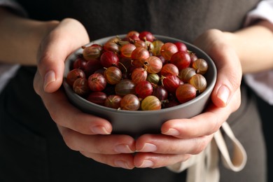 Photo of Woman holding bowl full of ripe gooseberries, closeup