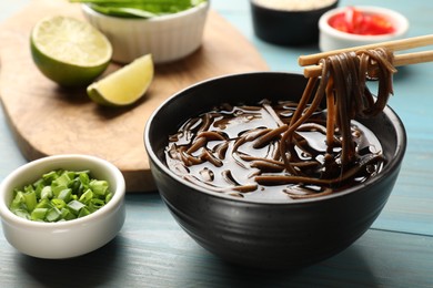 Photo of Eating delicious buckwheat noodle (soba) soup with chopsticks at light blue wooden table, closeup