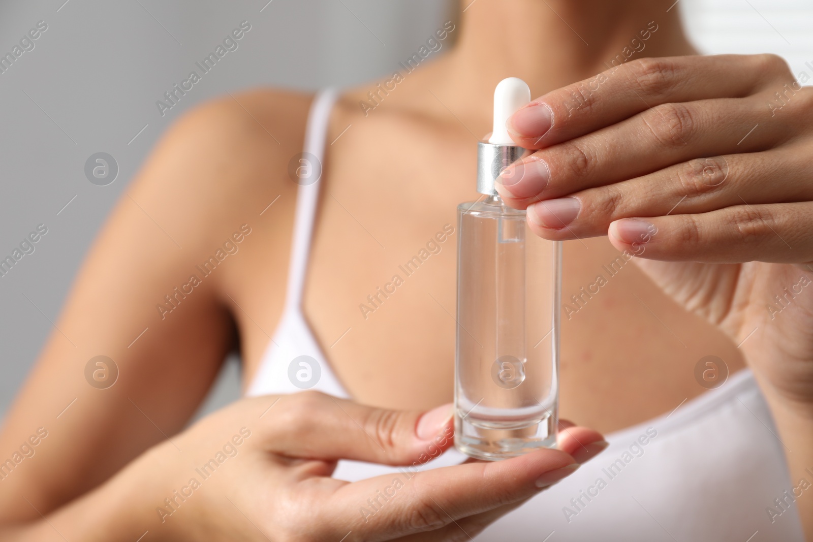 Photo of Woman with bottle of cosmetic serum on grey background, closeup