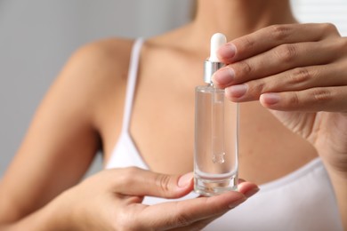 Woman with bottle of cosmetic serum on grey background, closeup