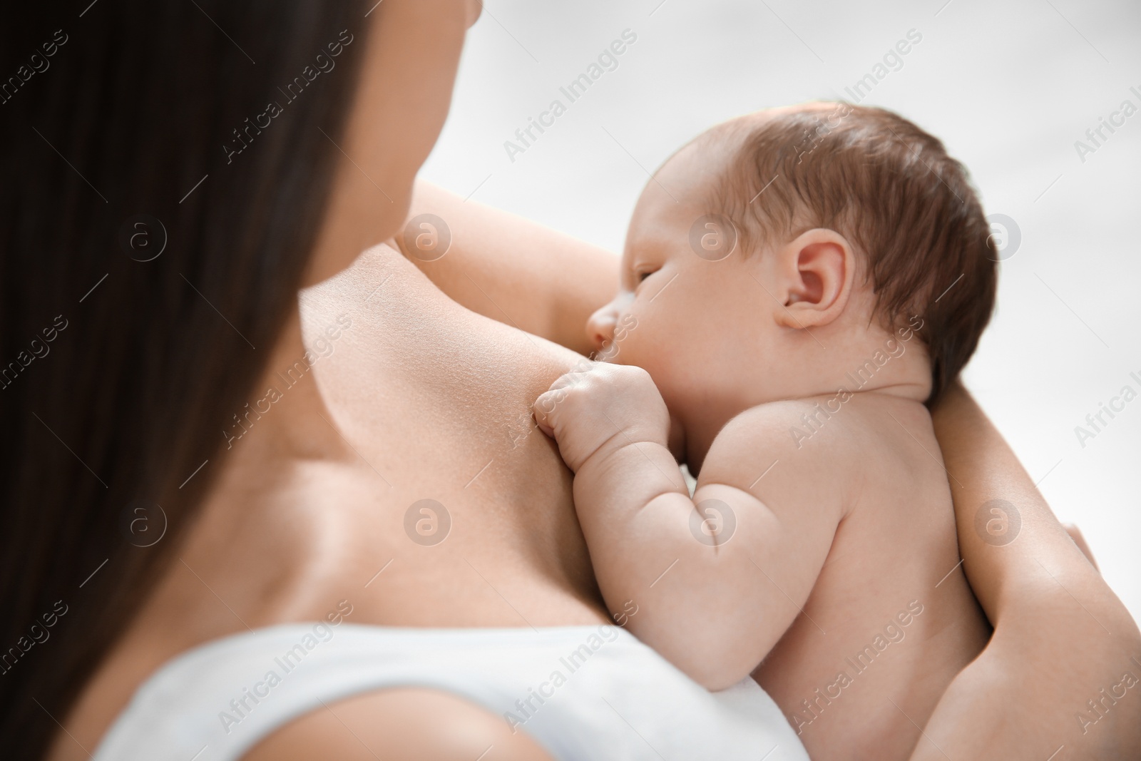 Photo of Young woman breastfeeding her baby on light background, closeup