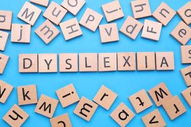 Photo of Wooden cubes with word Dyslexia on light blue background, flat lay