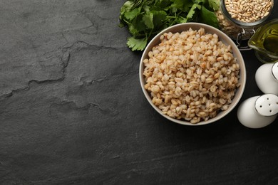 Photo of Tasty pearl barley porridge in bowl on dark textured table, flat lay. Space for text