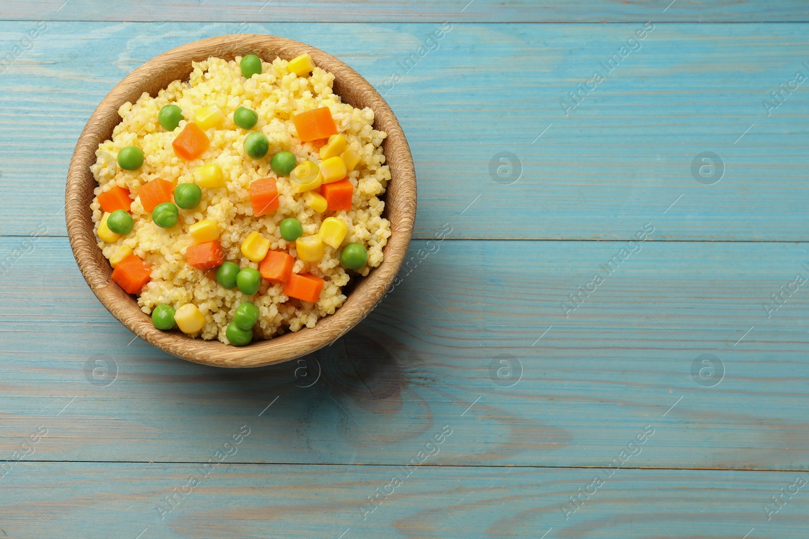 Photo of Tasty millet porridge with vegetables in bowl on light blue wooden table, top view. Space for text