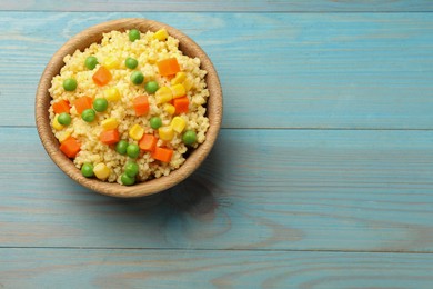 Photo of Tasty millet porridge with vegetables in bowl on light blue wooden table, top view. Space for text