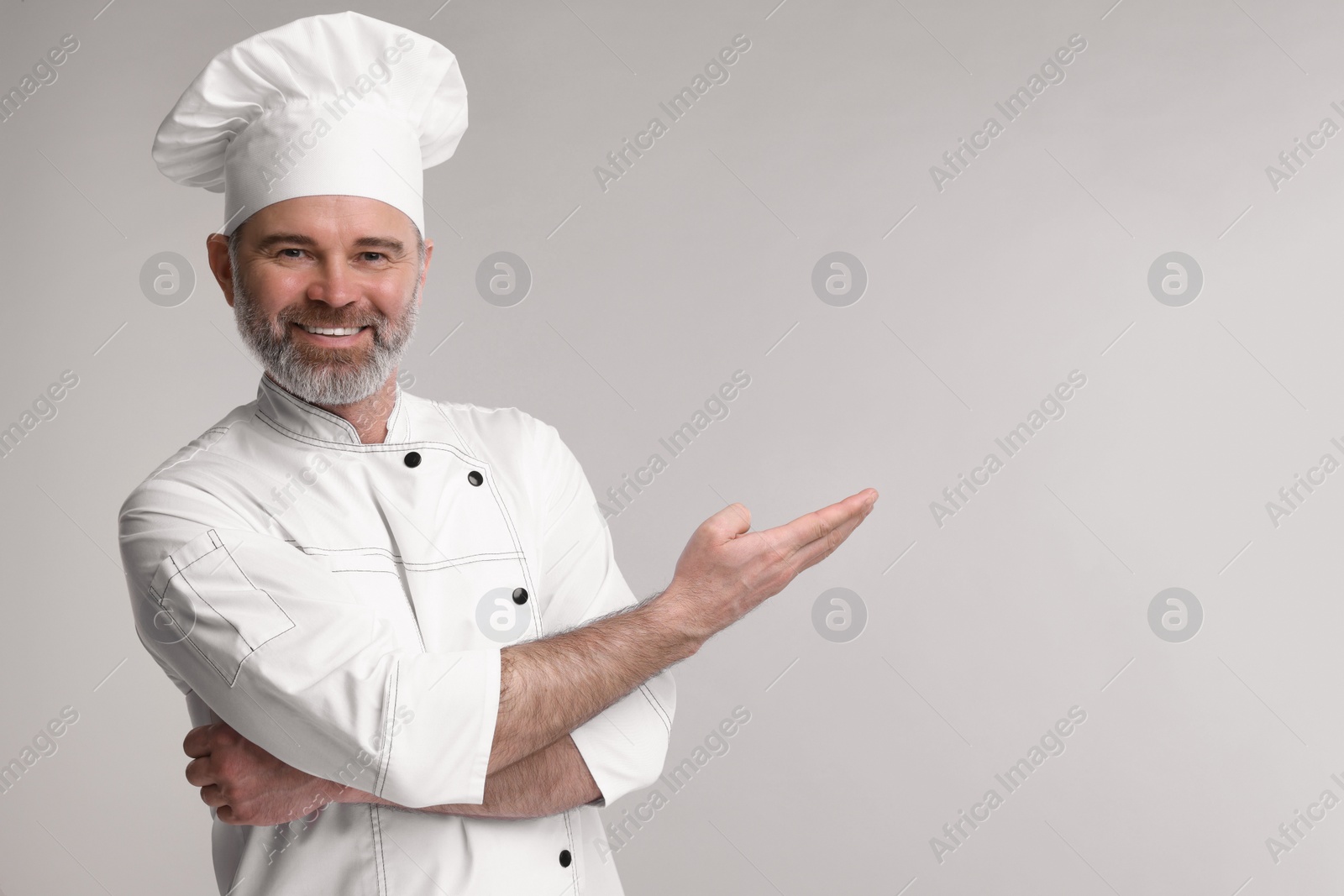 Photo of Happy chef in uniform showing something on grey background, space for text