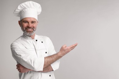 Happy chef in uniform showing something on grey background, space for text