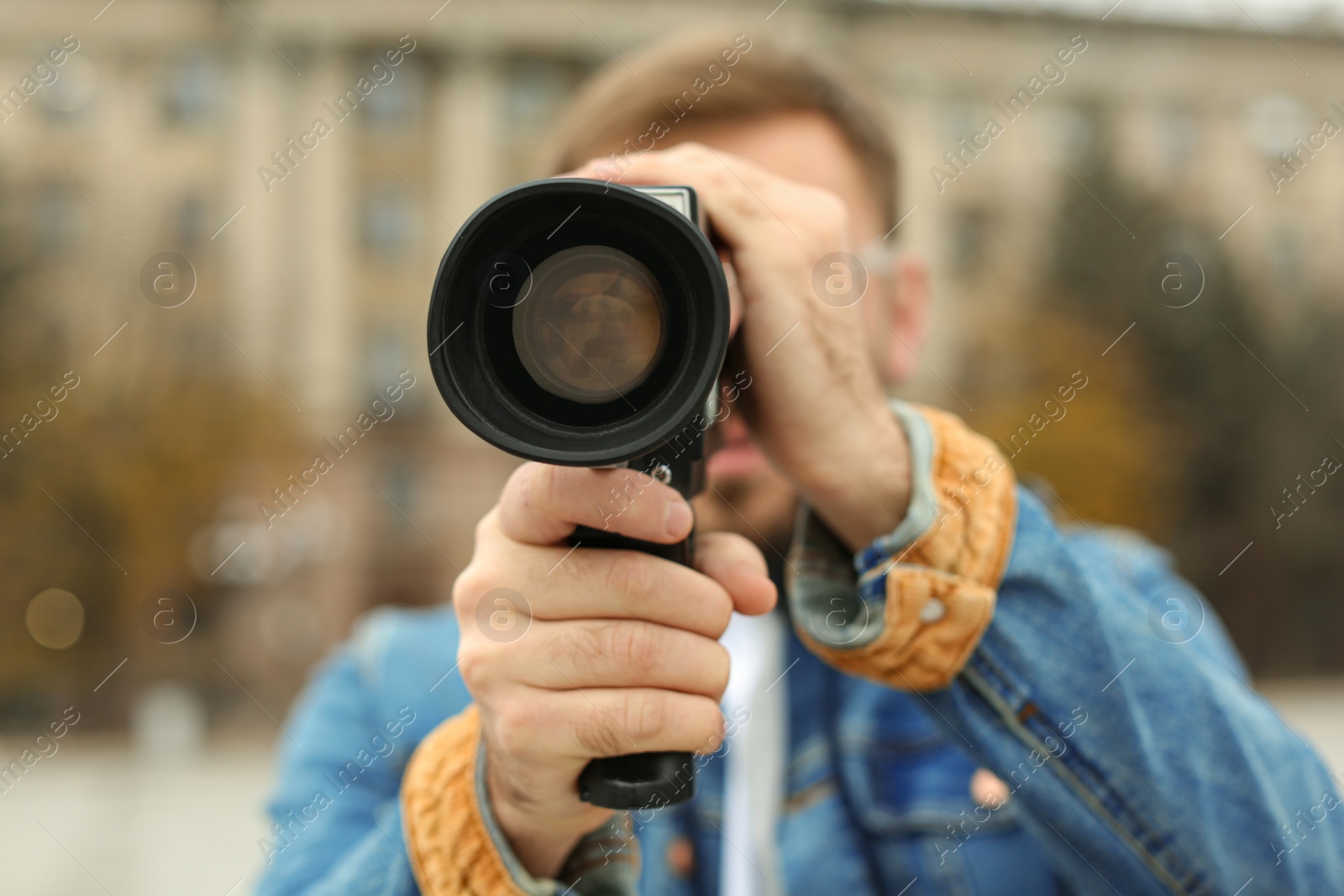 Photo of Young man with vintage video camera on city street, focus on lens