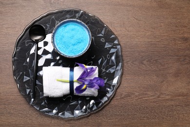 Photo of Light blue sea salt in bowl, flower, towel and spoon on wooden table, top view. Space for text