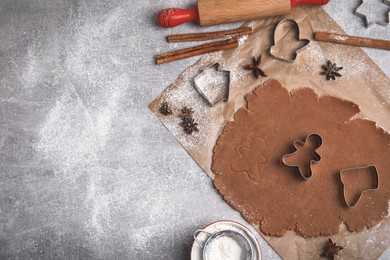 Photo of Making Christmas cookies. Flat lay composition with raw dough and cutters on grey table, space for text