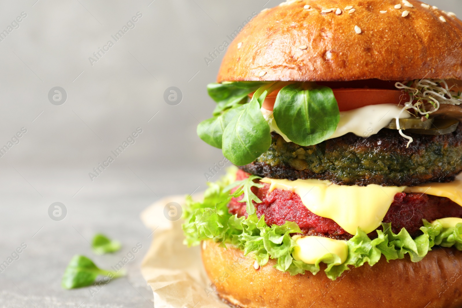 Photo of Vegan burger with beet and falafel patties on grey background, closeup