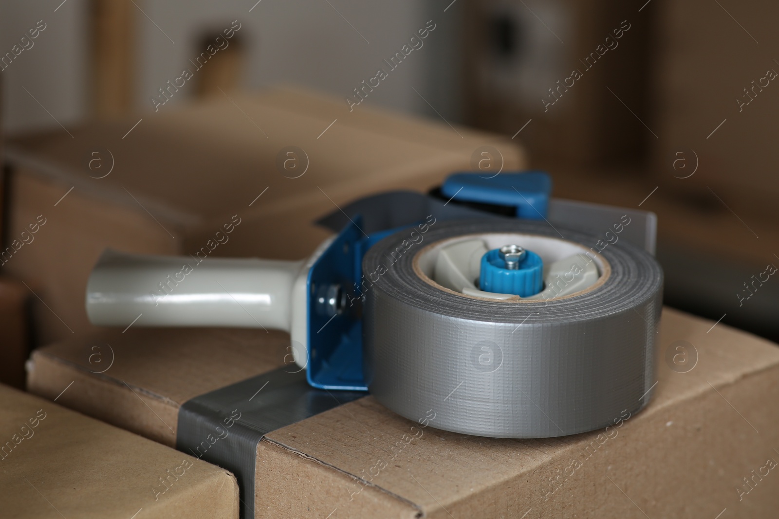 Photo of Adhesive tape dispenser on cardboard box indoors, closeup