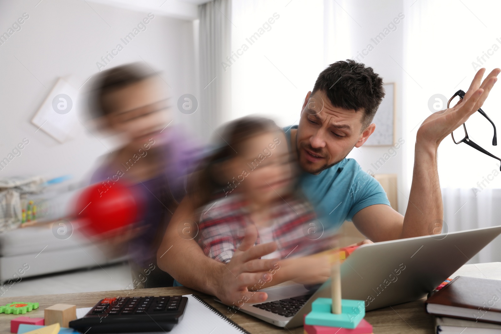 Image of Children disturbing overwhelmed man in living room. Working from home during quarantine