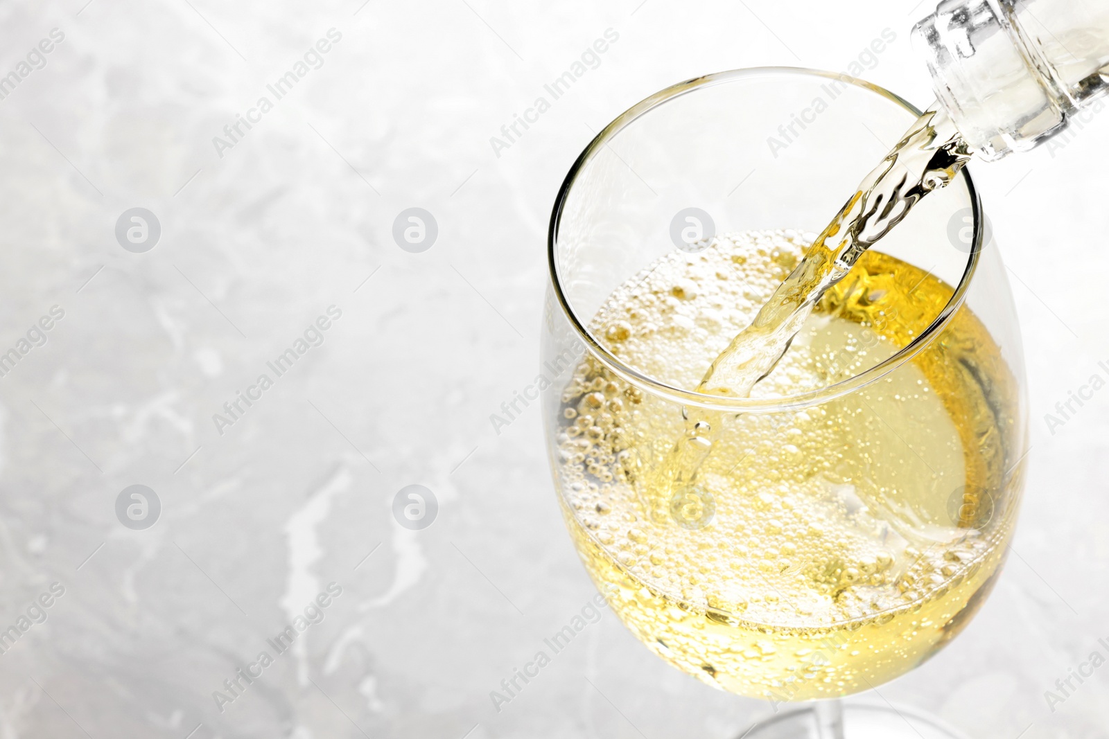 Photo of Pouring tasty aromatic wine in glass at gray marble table, closeup. Space for text