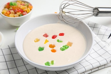 Photo of Raw dough with candied fruits for cookies and whisk on white table, closeup