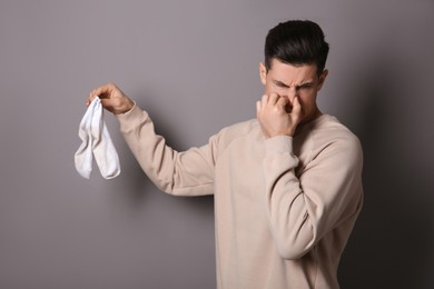 Photo of Man feeling bad smell from dirty socks on grey background