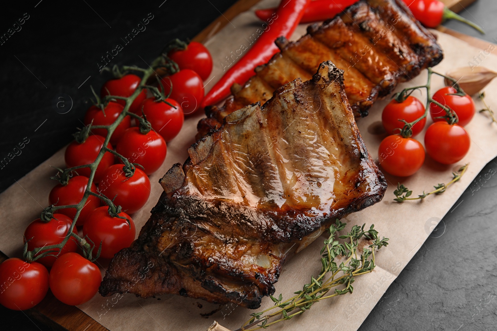 Photo of Tasty grilled ribs with tomatoes on black table