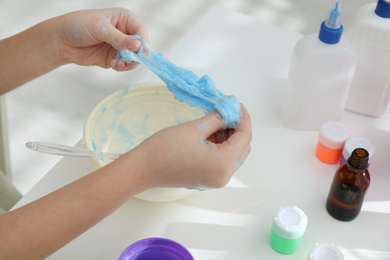 Photo of Little girl making DIY slime toy at table, closeup