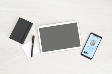 Online store website on device screen. Tablet, smartphone and stationery on white wooden table, flat lay