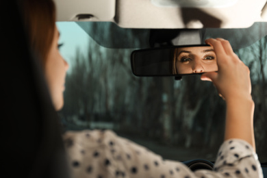 Young woman adjusting rear view mirror in car, closeup