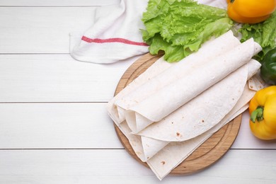 Photo of Delicious rolled Armenian lavash and fresh vegetables on white wooden table, flat lay. Space for text
