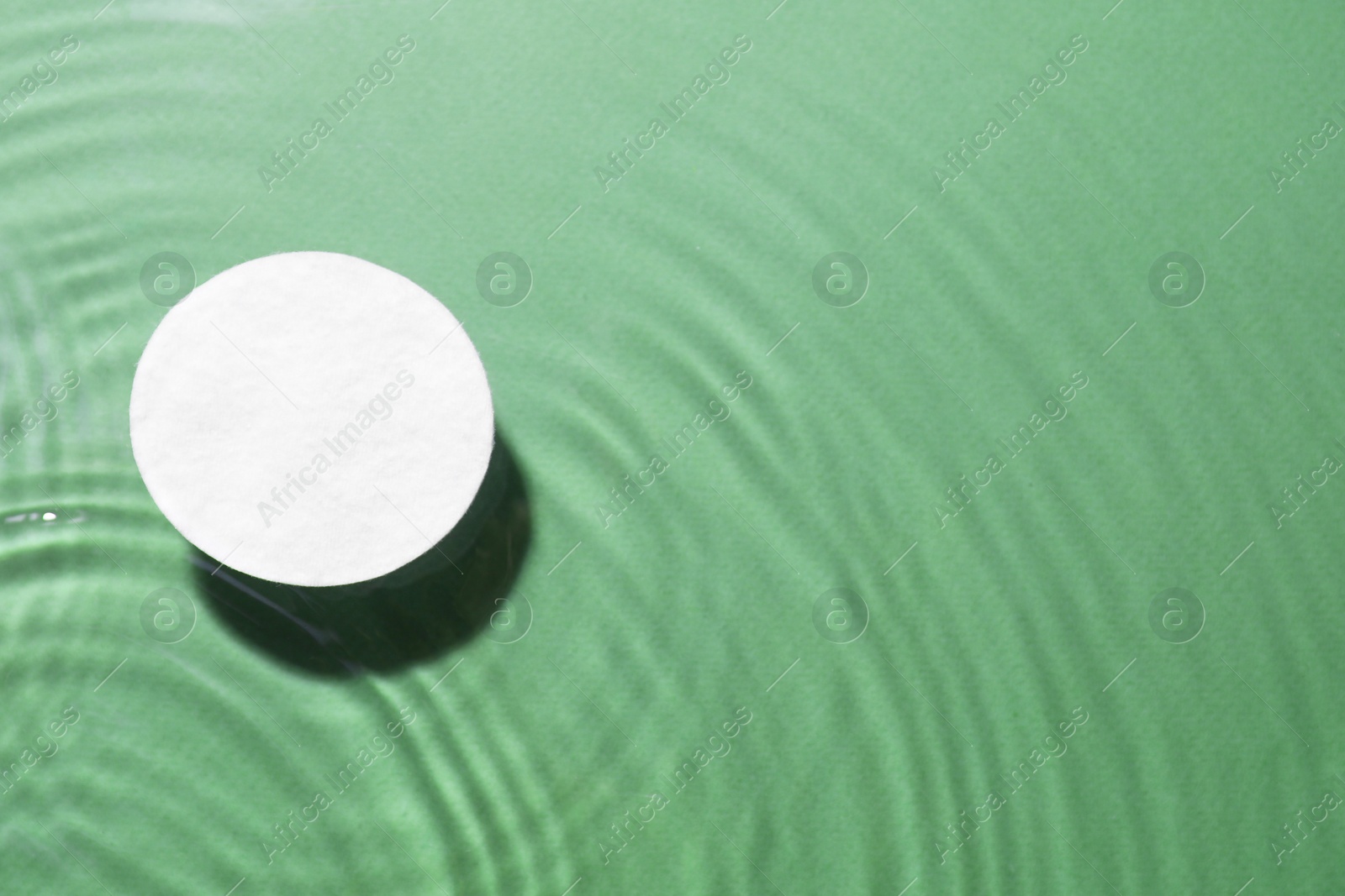Image of Cotton pad in micellar water on green background, above view. Space for text