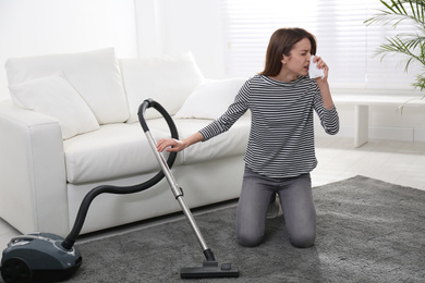 Photo of Young woman suffering from dust allergy while vacuuming house