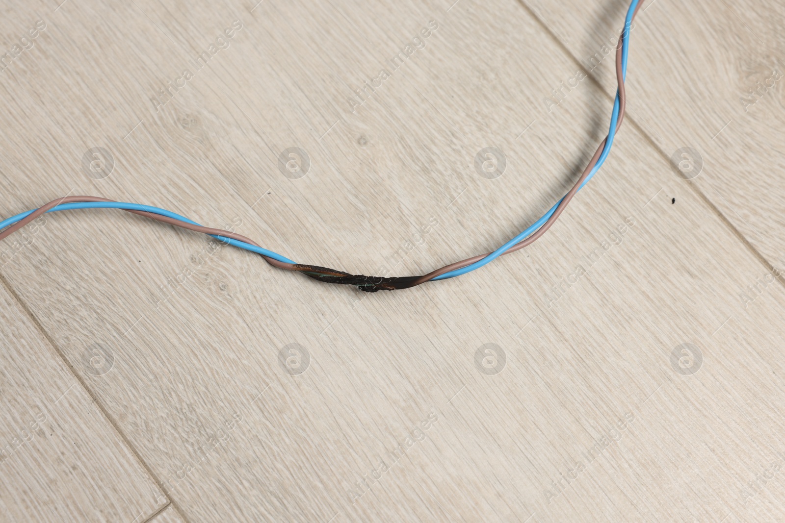 Photo of Burnt wires on wooden floor, above view. Electrical short circuit