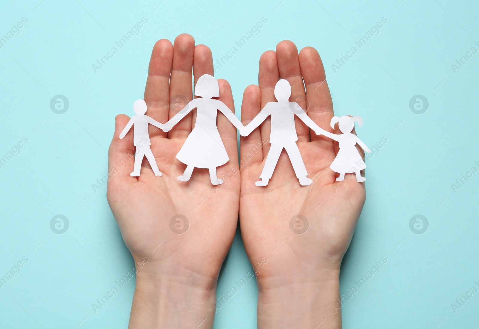 Photo of Woman holding paper cutout of family on light blue background, top view