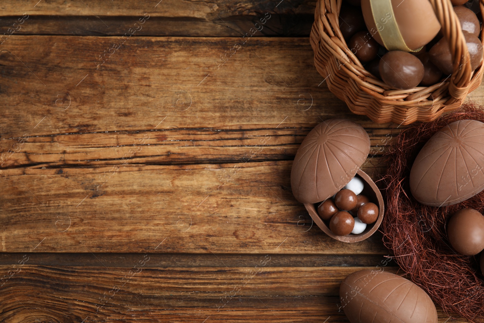 Photo of Flat lay composition with tasty chocolate eggs, wicker basket and decorative nest on wooden table. Space for text