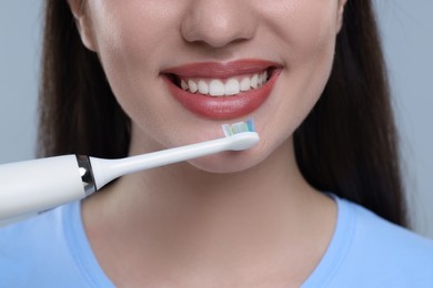 Photo of Woman brushing her teeth with electric toothbrush on light grey background, closeup