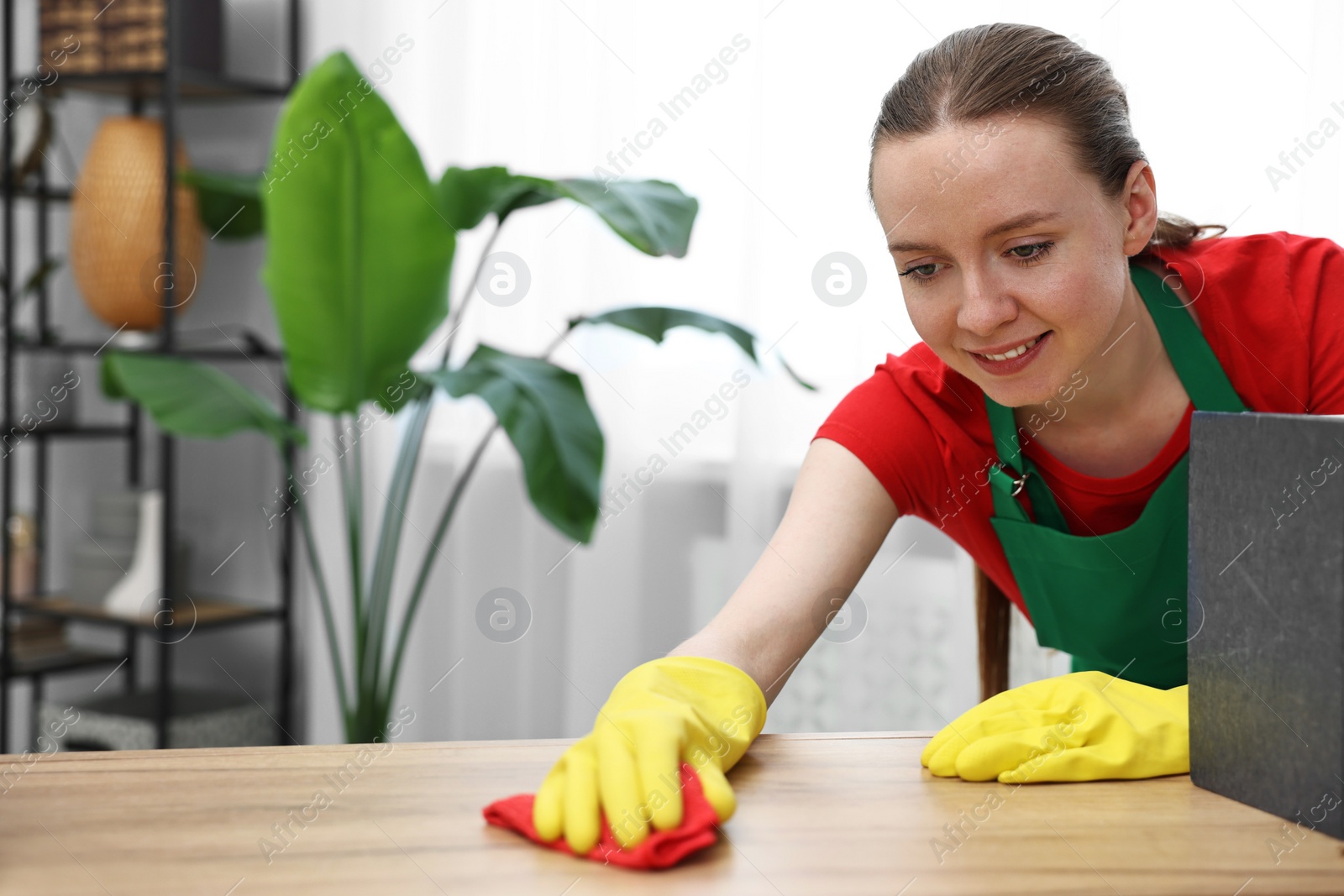 Photo of Woman cleaning wooden table with rag at home