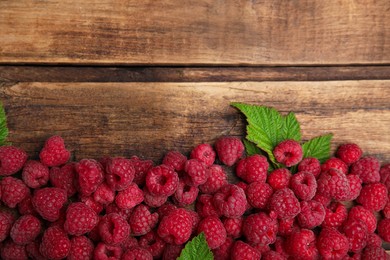 Photo of Fresh ripe raspberries with green leaves on wooden table, flat lay. Space for text