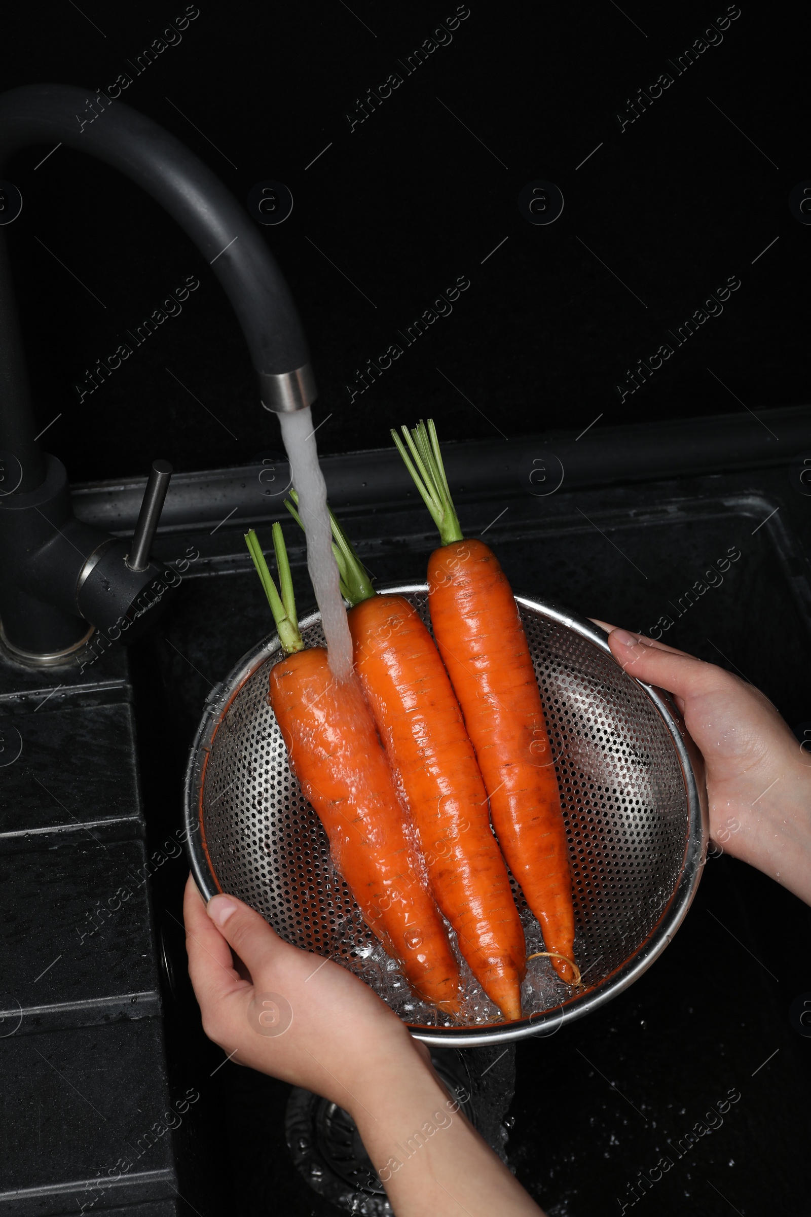 Photo of Woman washing fresh ripe juicy carrots under tap water in sink, above view