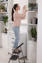 Photo of Woman on ladder watering houseplant at home