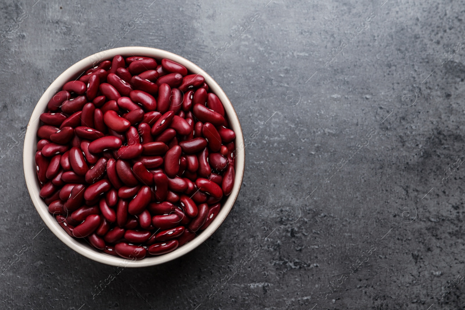 Photo of Raw red kidney beans in bowl on grey table, top view. Space for text