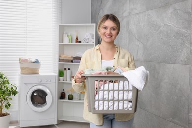 Photo of Happy woman with basket full of laundry in bathroom
