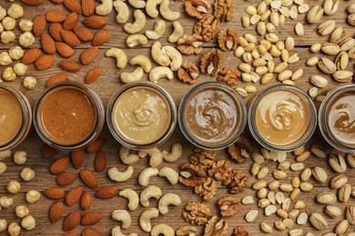 Nut butters in bowls and ingredients on wooden table, flat lay