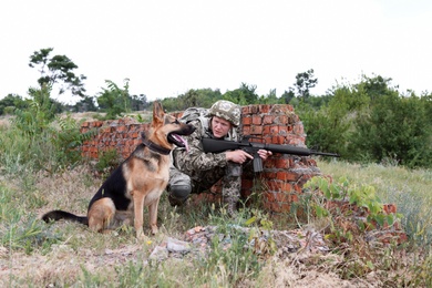 Man in military uniform with German shepherd dog near broken brick wall