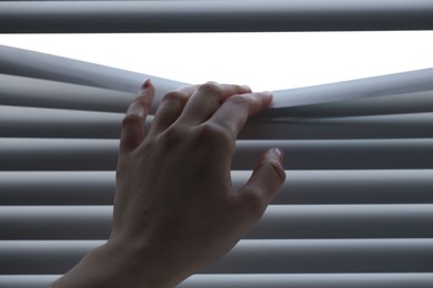 Woman separating slats of white blinds indoors, closeup