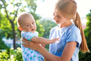 Teen nanny with cute baby outdoors on sunny day