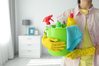 Photo of Woman holding bucket with different cleaning supplies at home, closeup. Space for text
